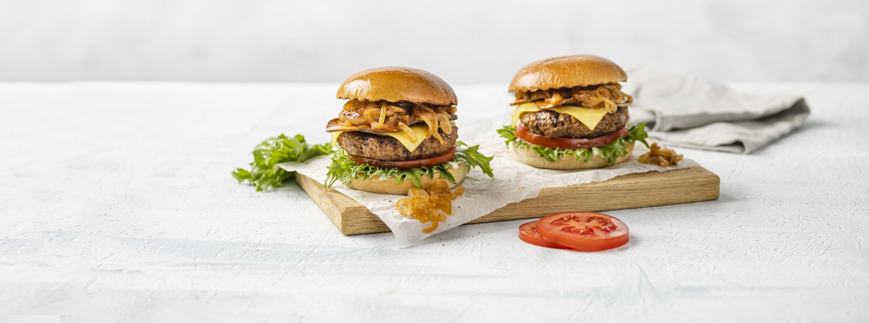 Two juicy plant-based hamburgers with fresh lettuce and tomato on a rustic wooden cutting board.