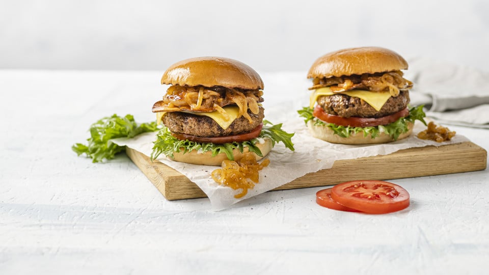 Two juicy plant-based hamburgers with fresh lettuce and tomato on a rustic wooden cutting board.