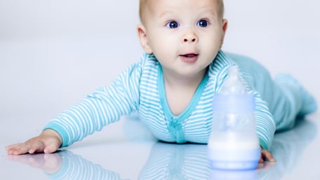 Happy baby on the floor, behind a feeding bottle - Special Nutrition - AAK