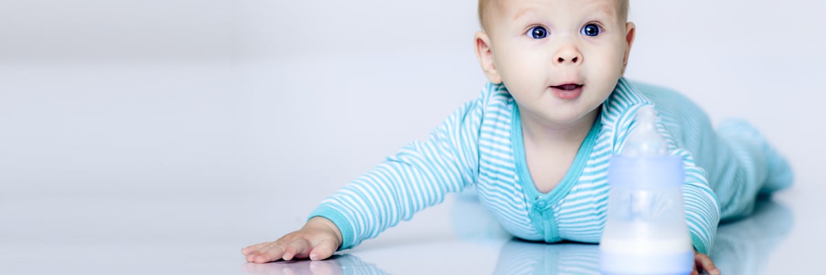 Happy baby on the floor, behind a feeding bottle - Special Nutrition - AAK