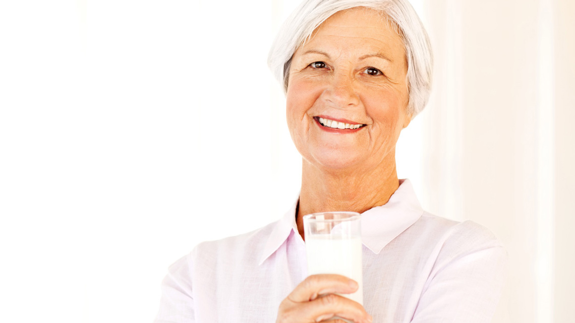 En äldre kvinna som ler och håller ett glas mjölk - Special Nutrition - AAK