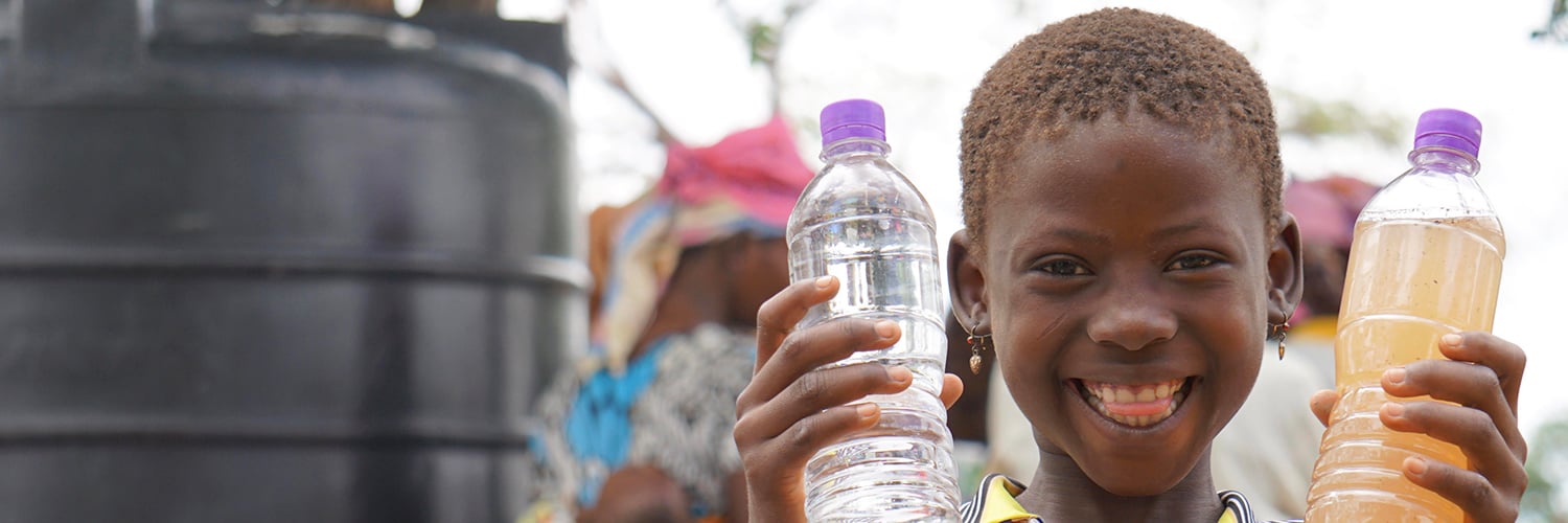 Young ghanaian girl holding bottles of clean and dirty water.