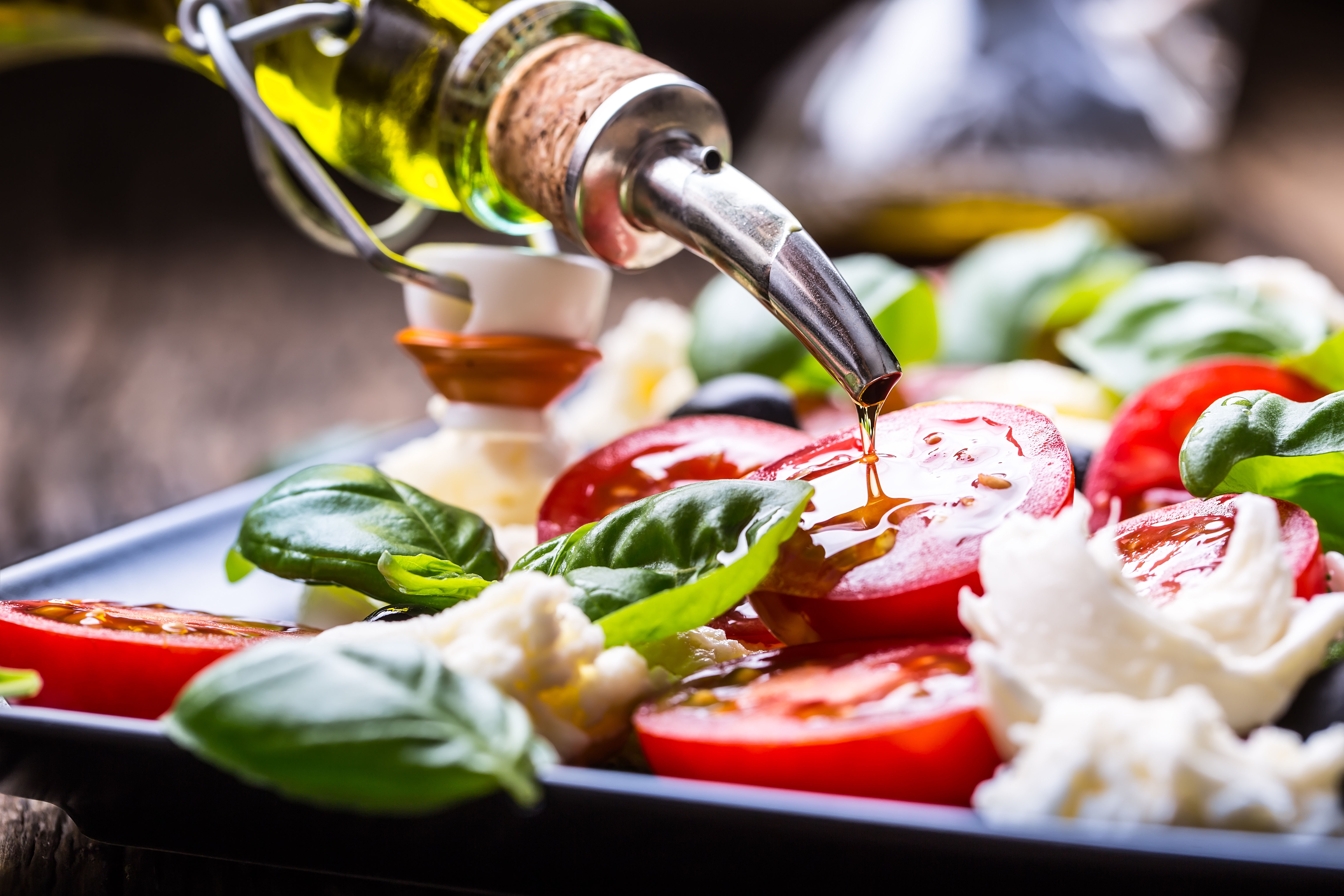 drizzling olive oil over a caprese salad made with tomatoes, mozzarella, and basil