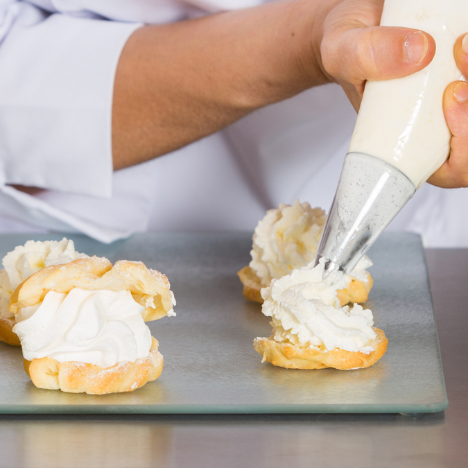 En bagare som spritsar grädde på bakelser - Mejeriprodukter och glass - AAK