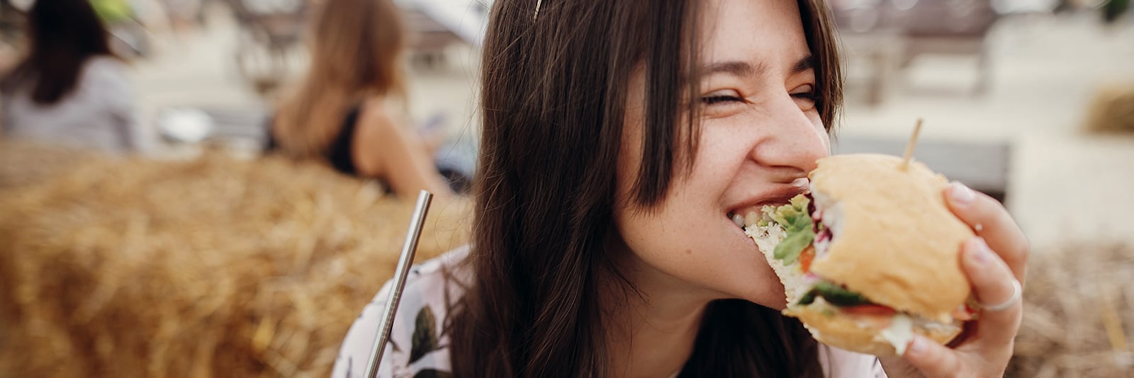 Kvinna njuter av en burgare i utomhusmiljö.