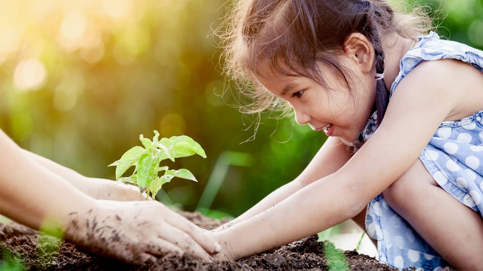 Child gardening with her parent while smiling.