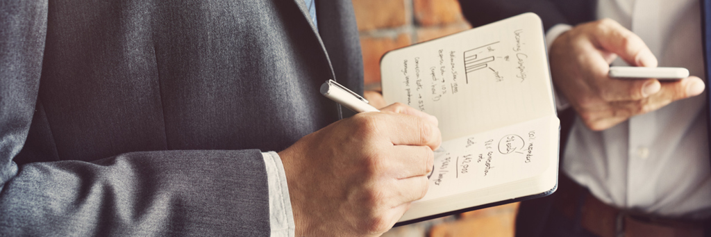 Businessmen Analysing and Writing News in a Note Book - Media - AAK