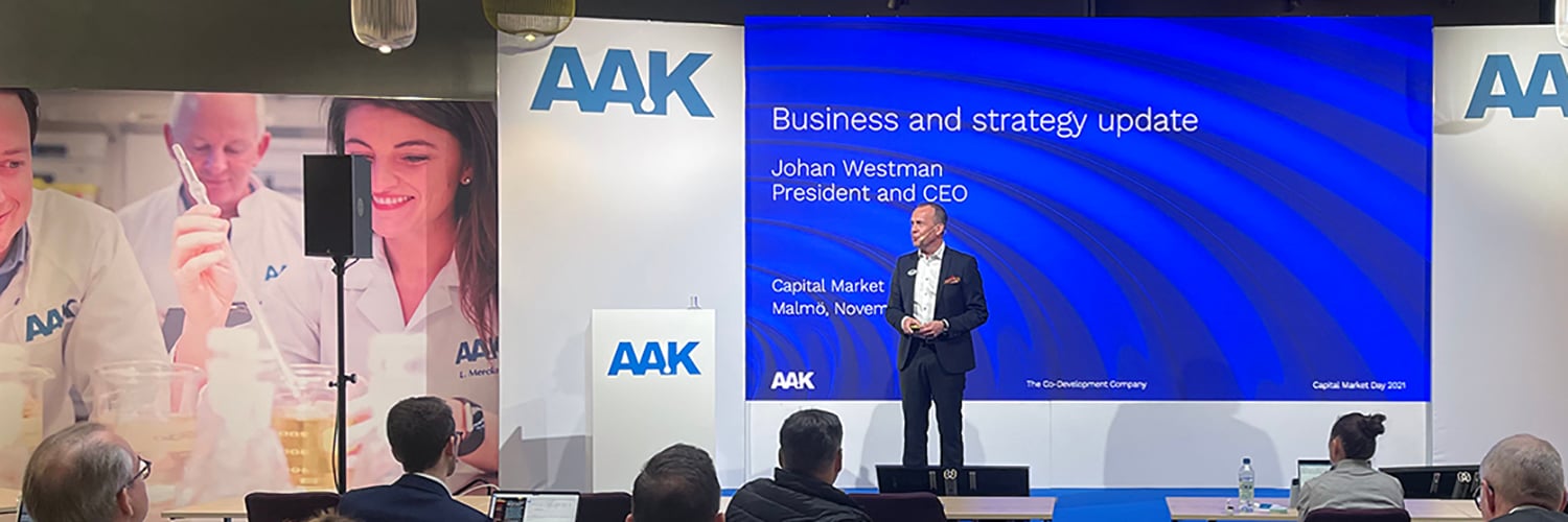 CEO Johan Westman, on stage presenting with AAK logo on screen and podium, audience seated in front.