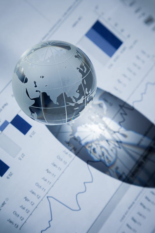 Glass globe placed on financial documents with bar and line charts, casting a shadow over parts of the charts.