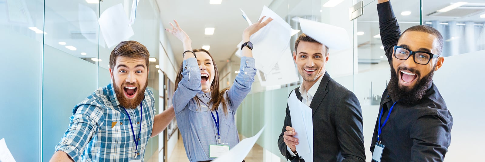 Fyra glada personer i en kontorskorridor kastar papper i luften.