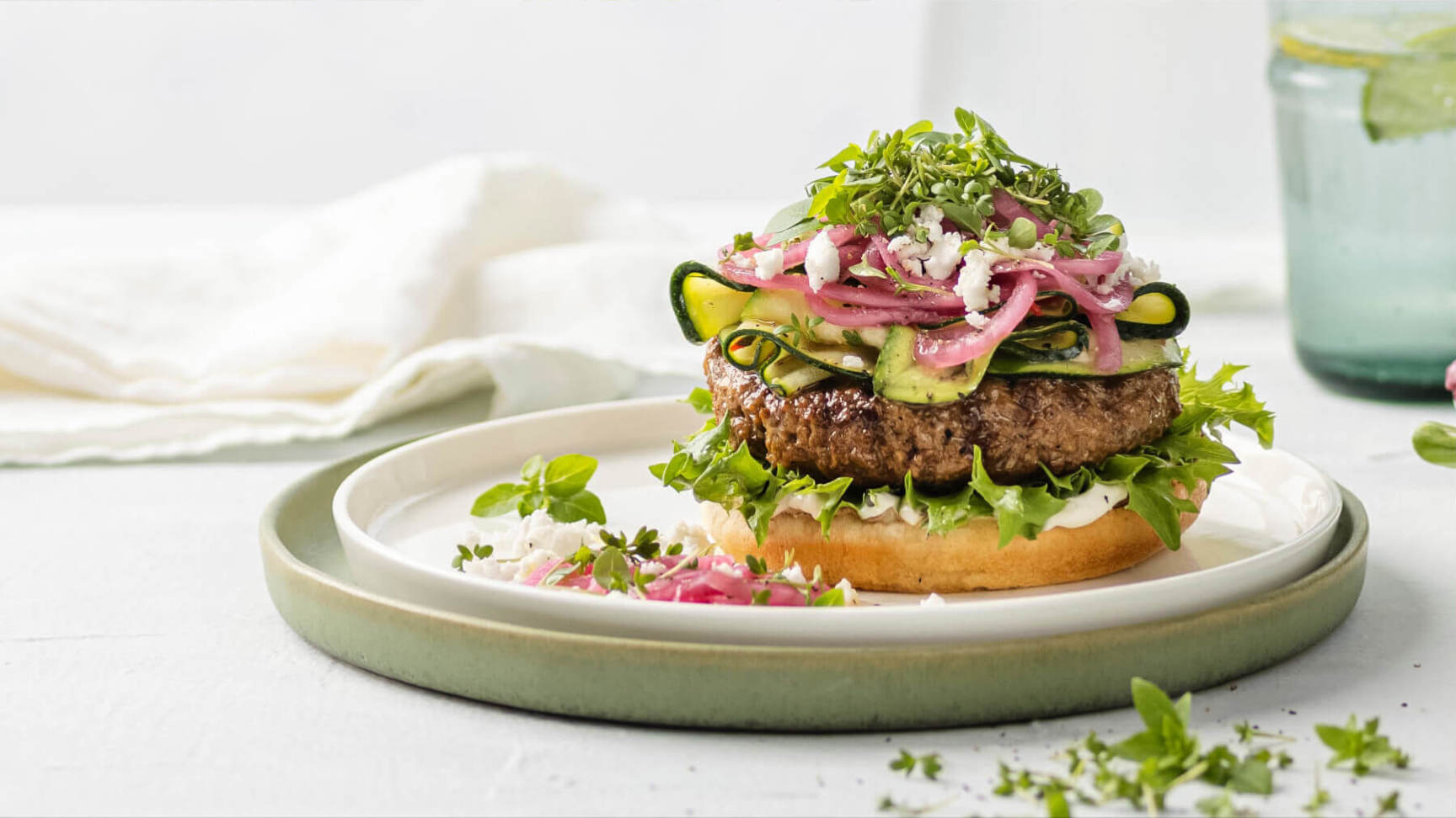 A juicy hamburger made with plant based meat, filled with vegetables next to a glass of water.