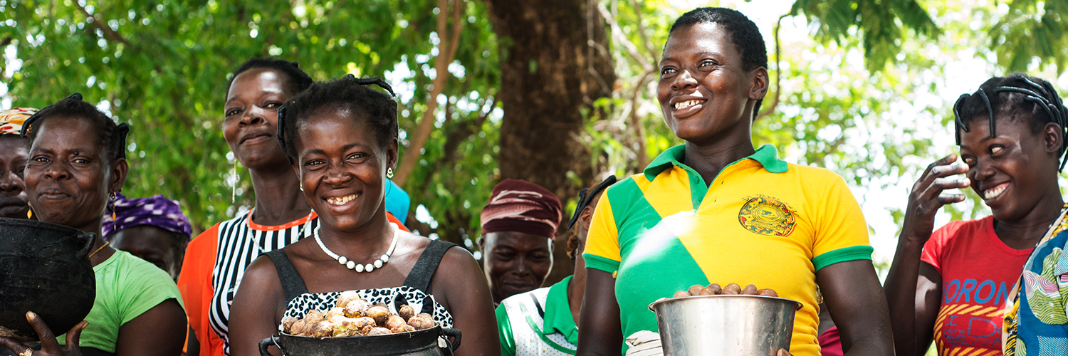 West african women standing outdoors holding bowls with shea kernels.