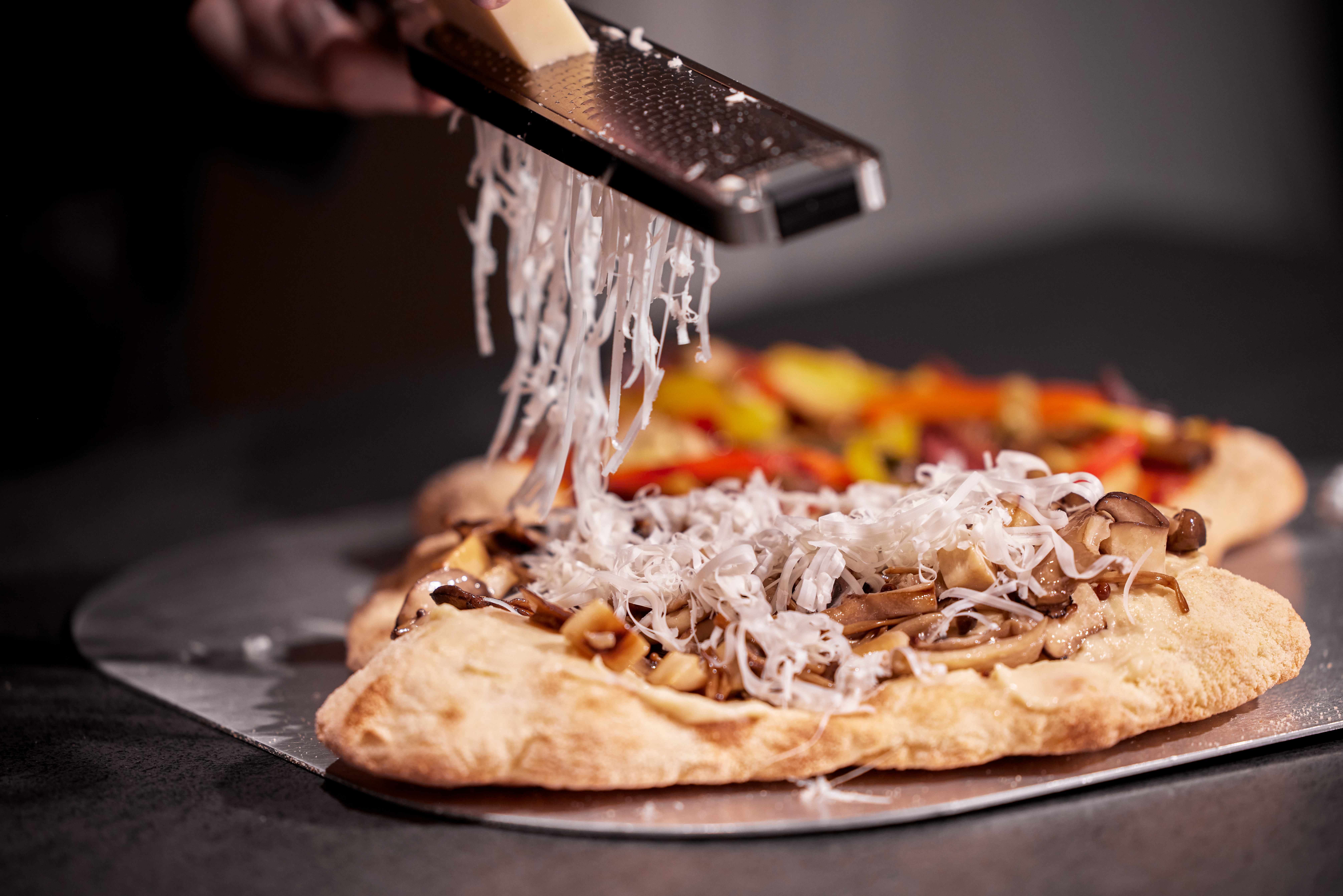 Grated cheese falls from a grater onto a mushroom‑topped pizza.
