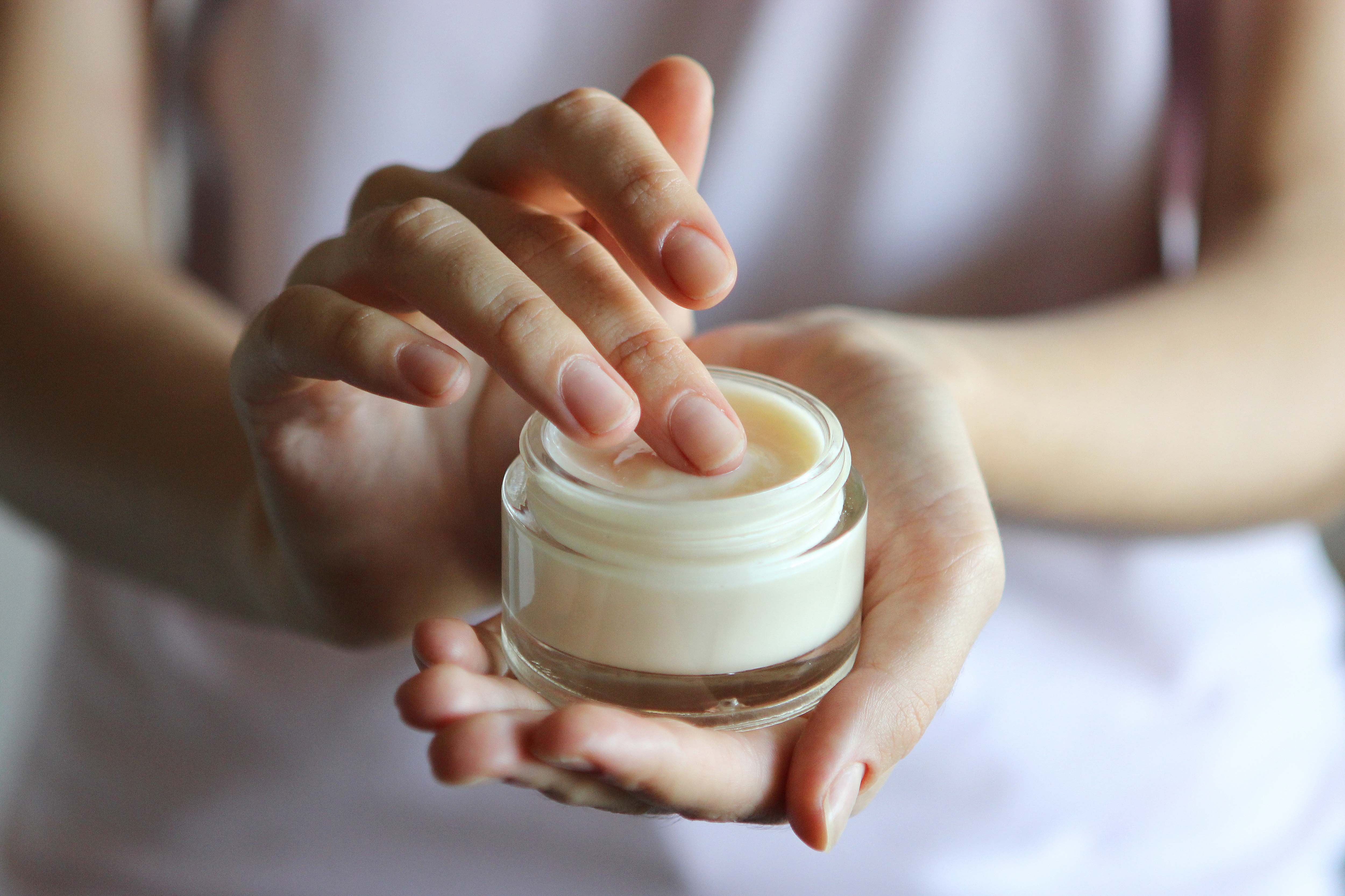 Hands applying cream from a small jar.