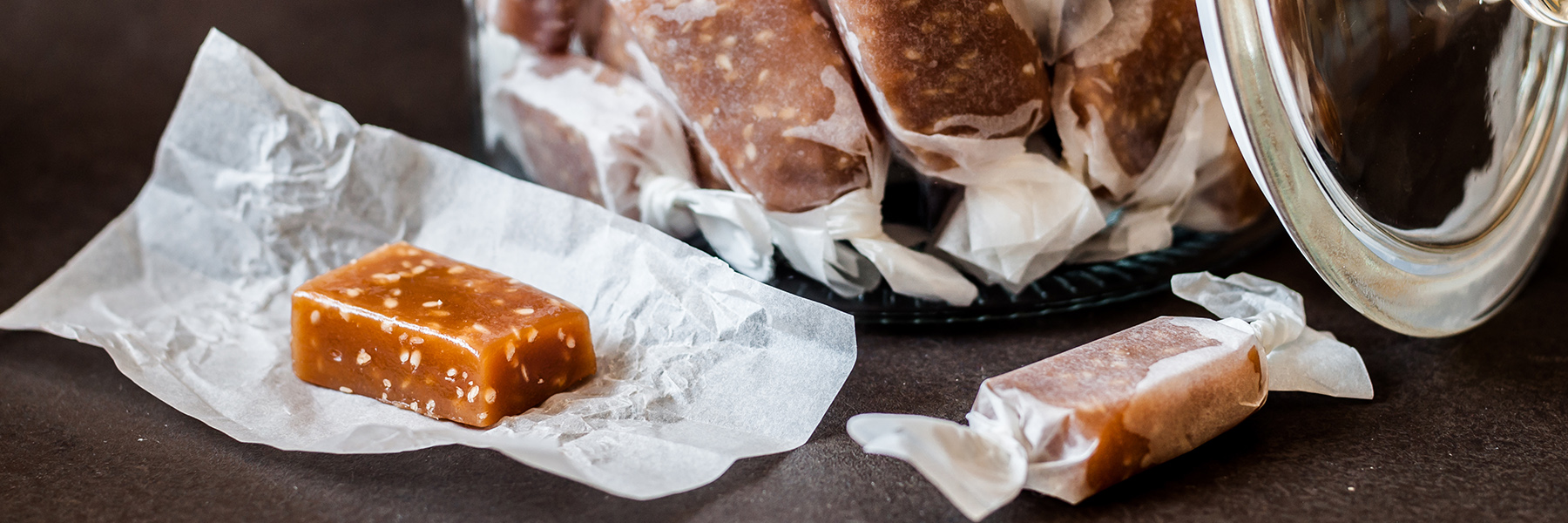 Close-up of caramel toffees, some wrapped and some unwrapped, with a jar in the background.