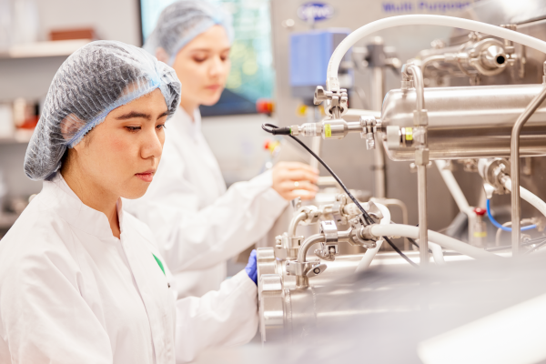 Two women in white lab coats collaborating on a complex machine in a laboratory setting.