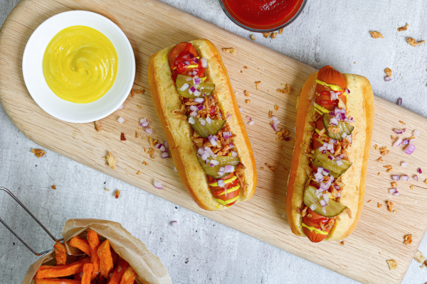 Two hot dogs made of plant based meat placed side by side on a wooden cutting board.