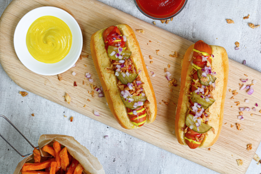 Two hot dogs made of plant based meat placed side by side on a wooden cutting board.