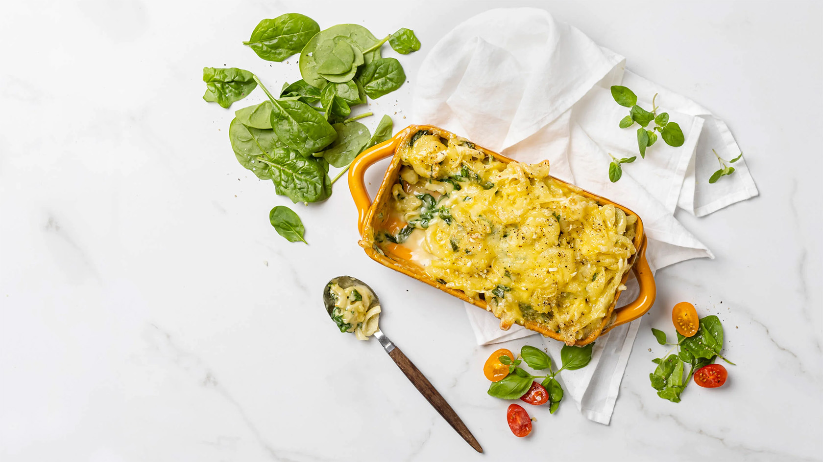 A spinach and cheese casserole served with a spoon beside a bowl of fresh spinach.