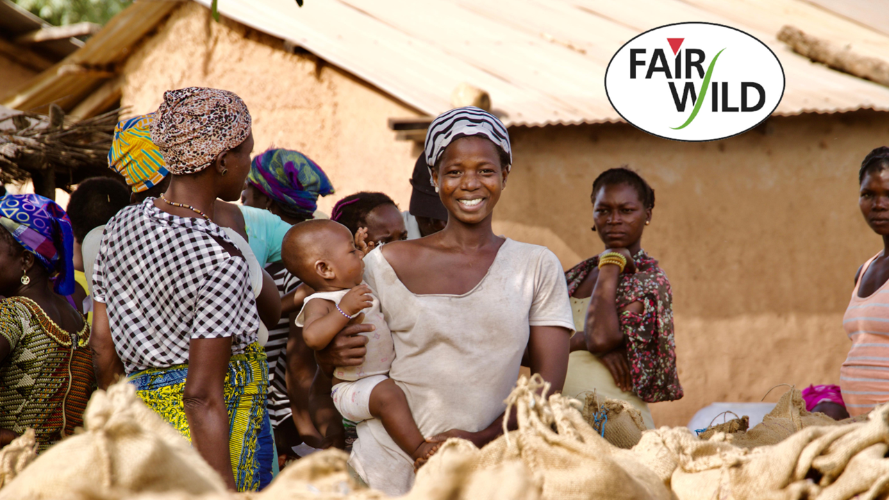 Group of african women standing outdoors , with one person holding a child and a FairWild certification logo in the corner.