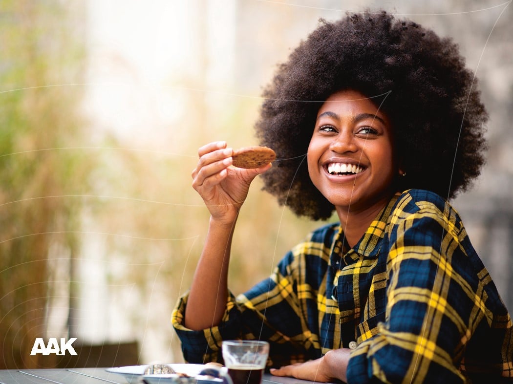 Person sitting by a table holding a cookie with a glass of espresso outdoors.