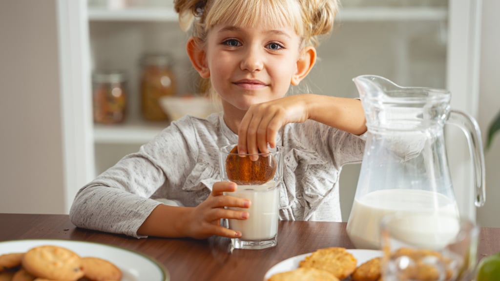 Little girl dunking a biscuit in a glass of milk.