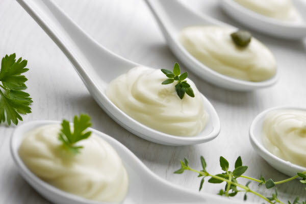 White ceramic spoons with creamy white sauce, some garnished with green herbs.