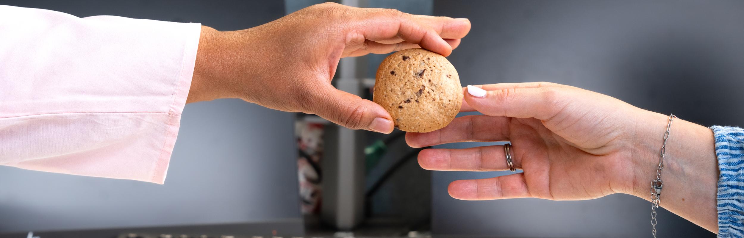 One persons giving another person a cookie where only hands are visible.